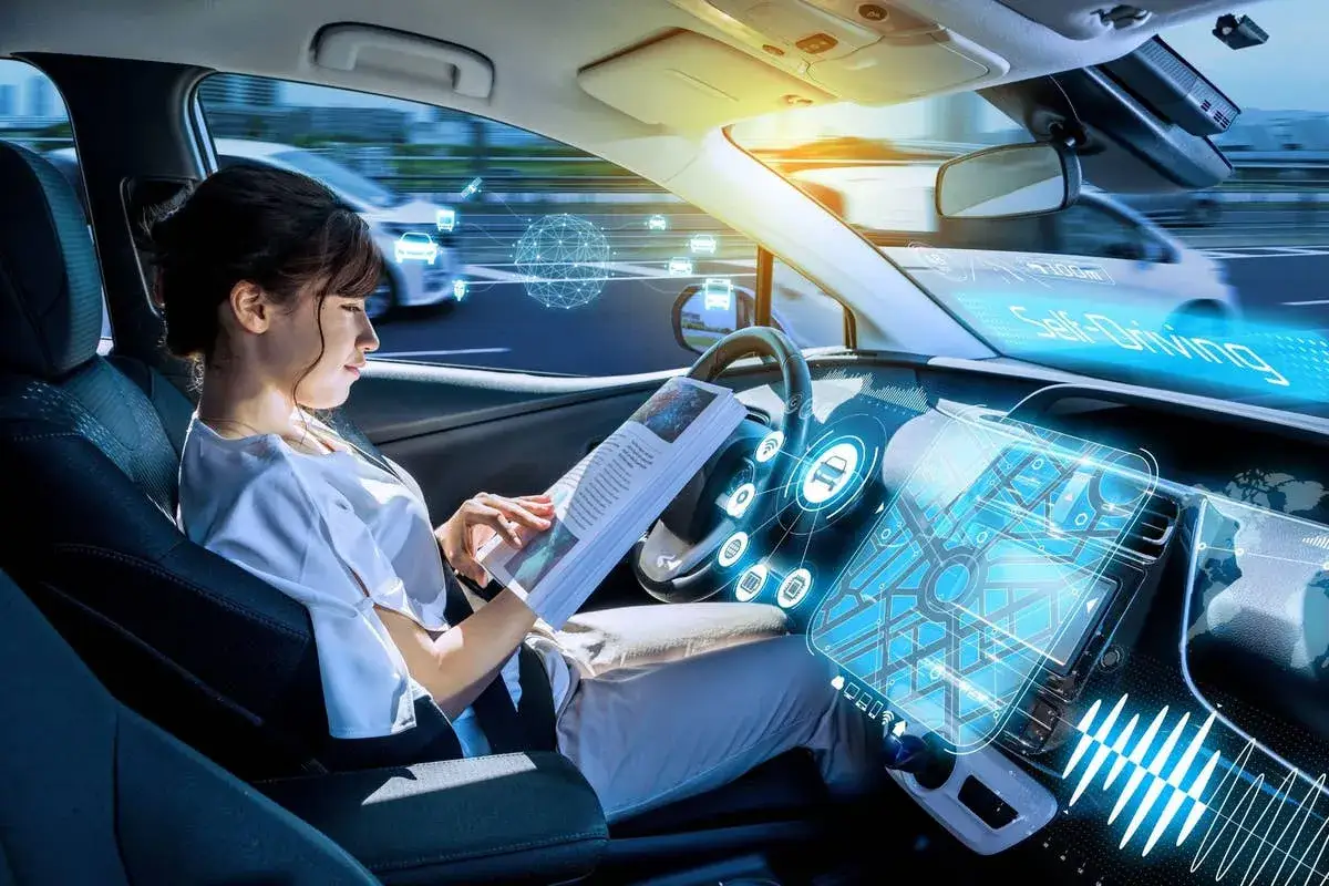 Donna legge un libro mentre l'auto viaggia in modalità guida autonoma livello 2, con interfaccia futuristica e dati di navigazione.
