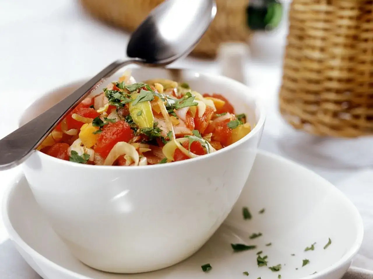 Frischer tomatensalat mit zwiebeln, garniert mit Kräutern, in einer weißen Schüssel mit Löffel.