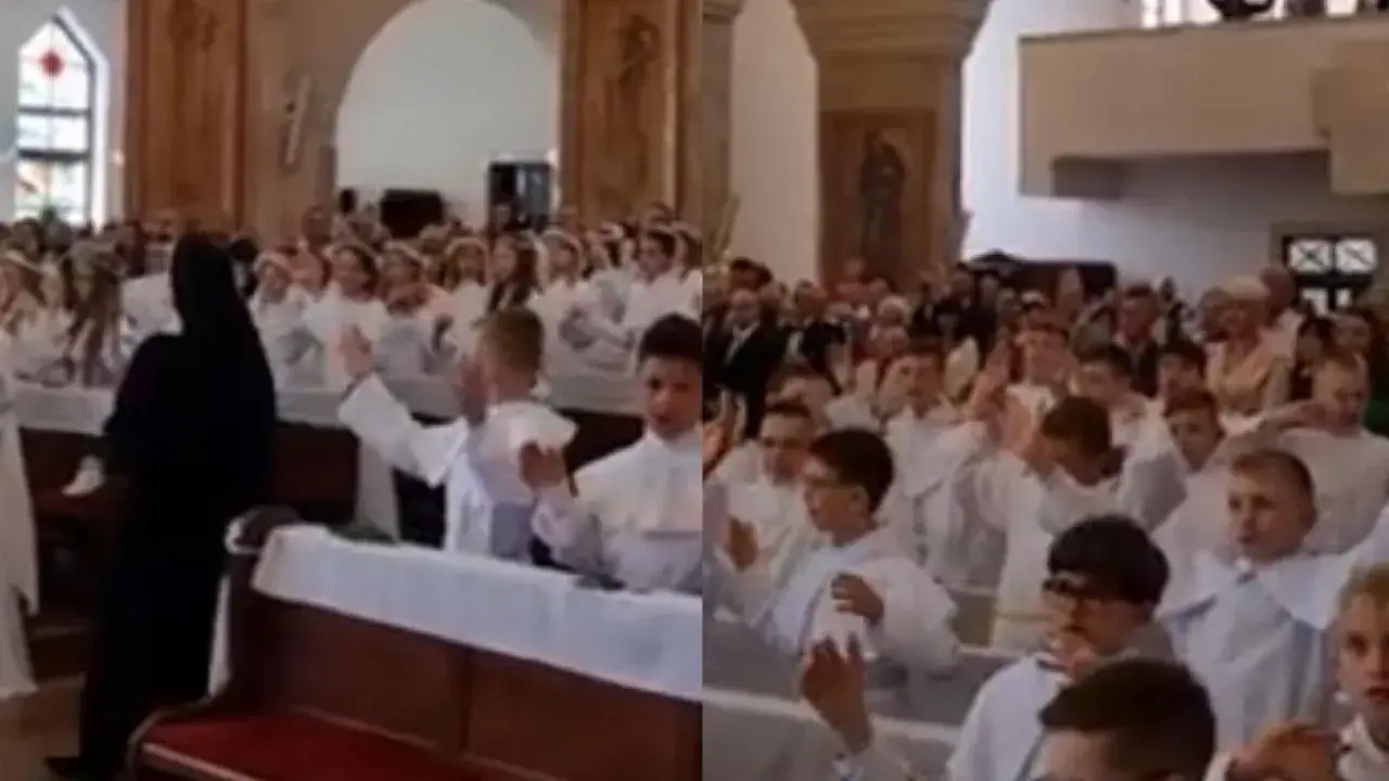 Dzieci w bieli śpiewają pieśni komunijne w kościele. Widać też siostrę zakonną i zgromadzonych wiernych.