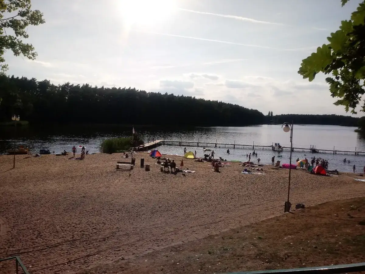 Plaża nad jeziorem, ludzie odpoczywają, dzieci kąpią się, w tle las. Idealne miejsce na wakacje w Jarosławkach.