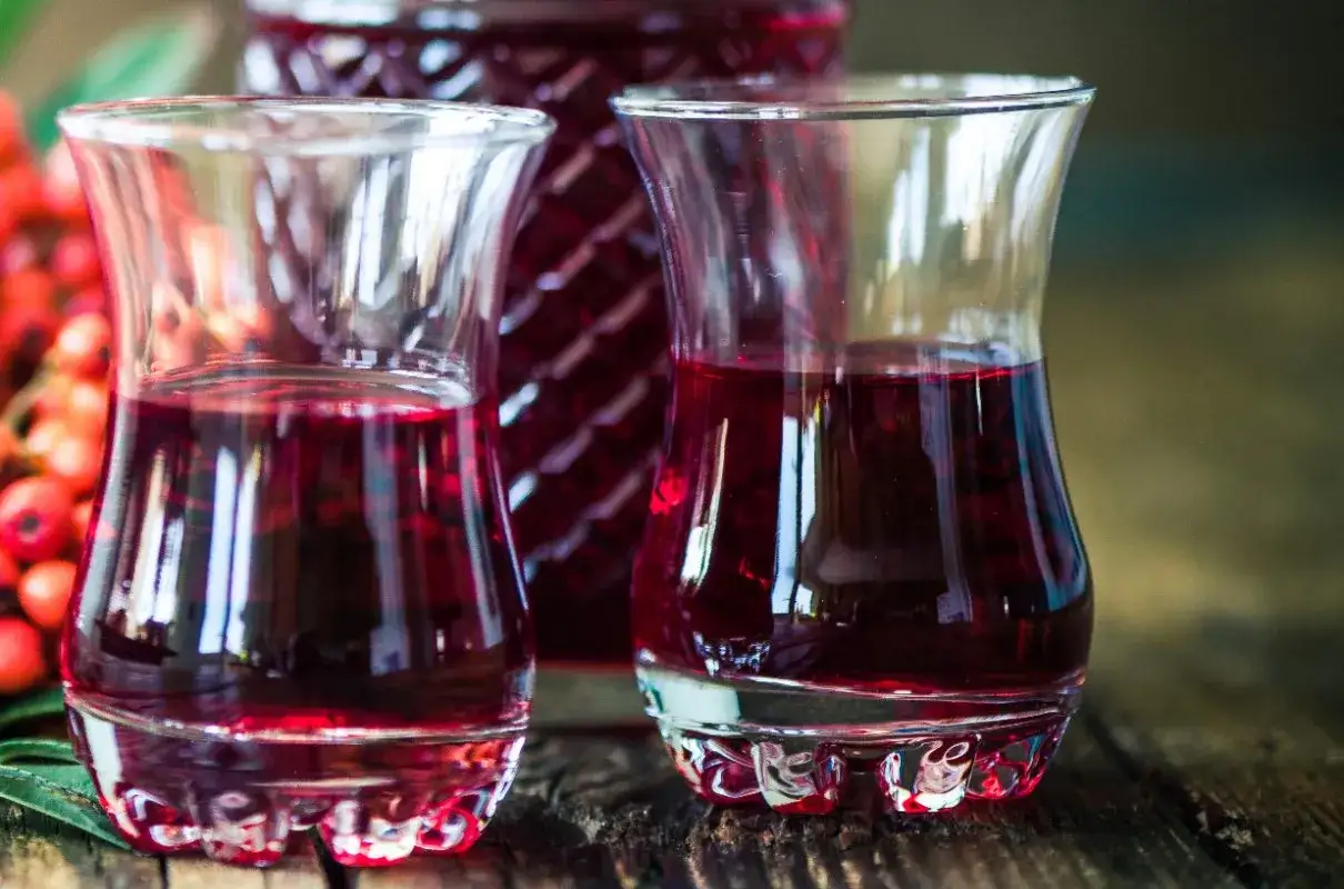 Dwa kieliszki wypełnione rubinową nalewką z czeremchy, obok butelka i kiście owoców.