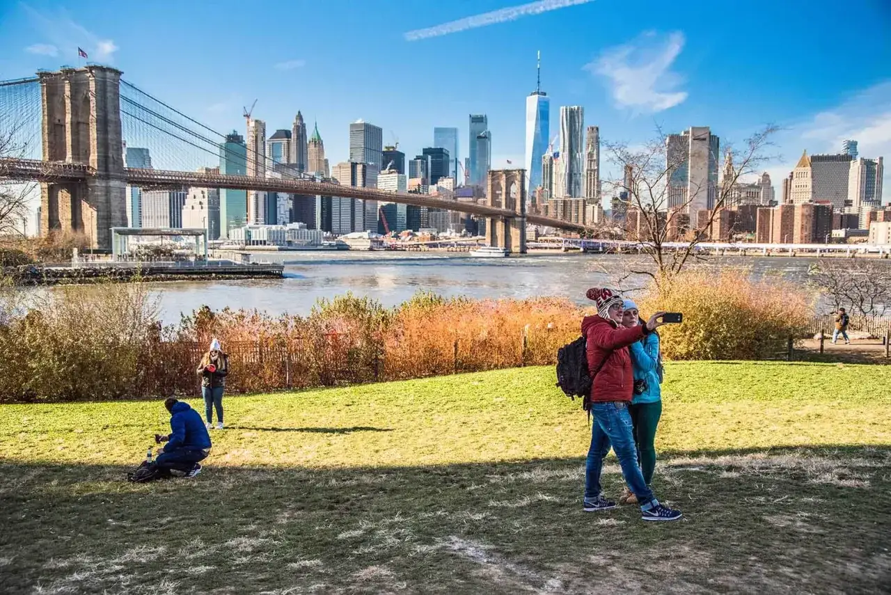 Widok na Manhattan z Brooklyn Bridge. Dwie osoby robią sobie selfie na tle panoramy miasta.