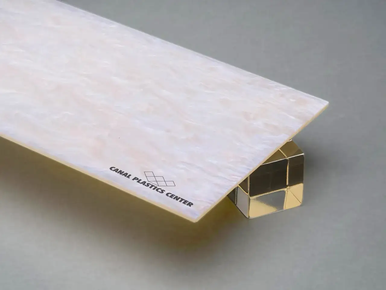 Un aperçu de ce qu'est une couleur irisée : une plaque nacrée aux reflets changeants repose sur un cube métallique brillant.