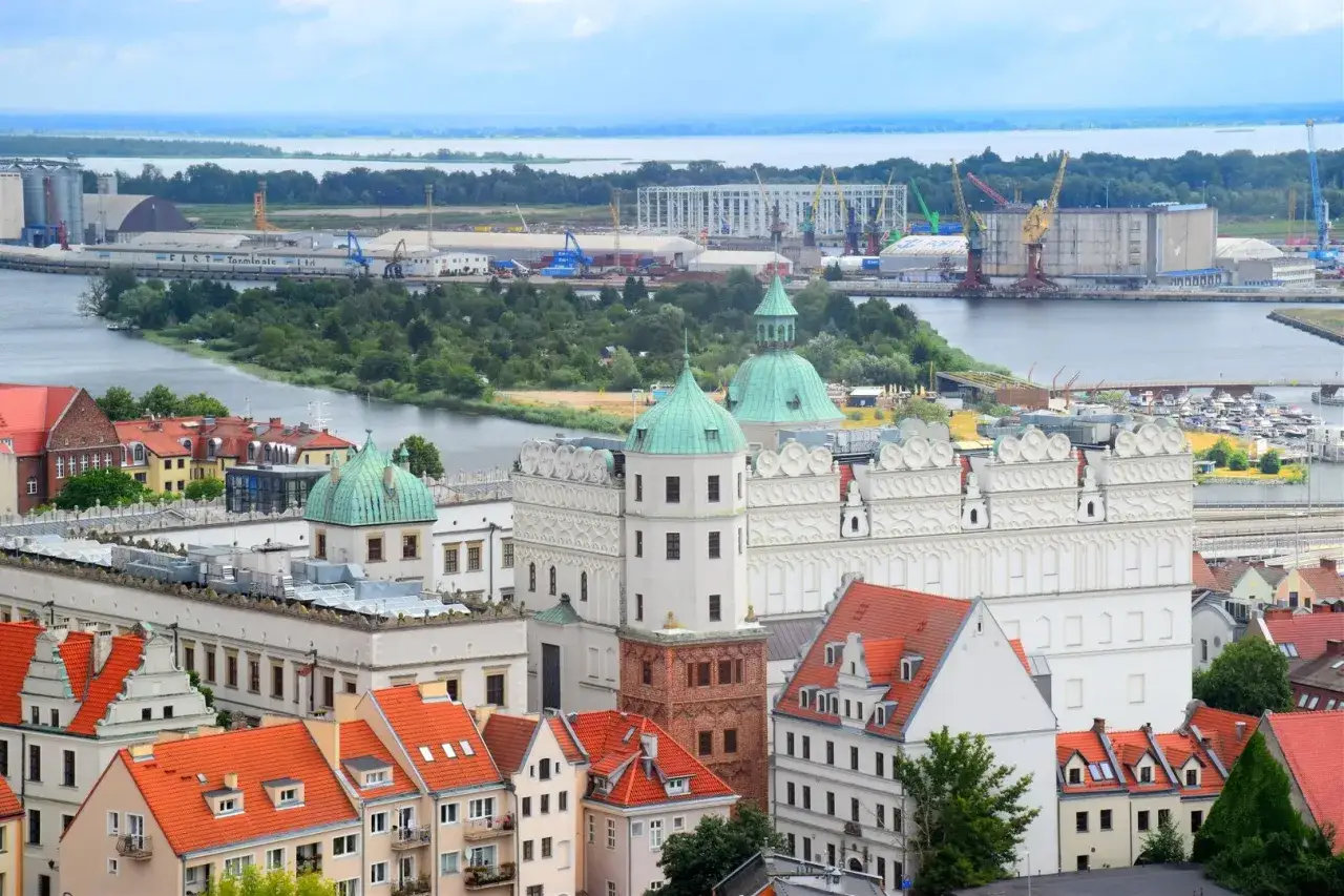 Widok na zamek i port w Szczecinie. W oddali widać portowe atrakcje, dźwigi i statki.