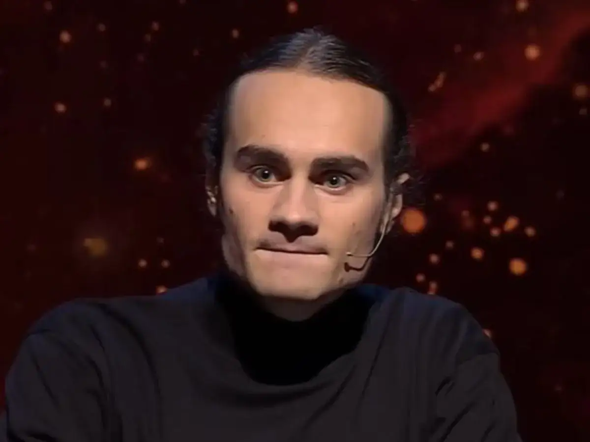 Artur 1 z 10, zamyślony, z mikrofonem przy uchu, na tle rozmytych świateł.