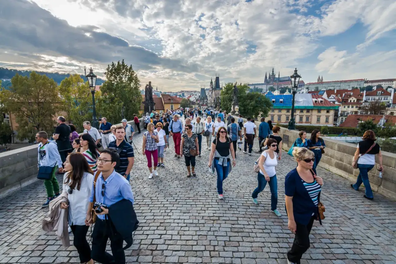 A lively Prague free walking tour on a cobblestone bridge, with tourists admiring the cityscape and historic architecture under a cloudy sky.