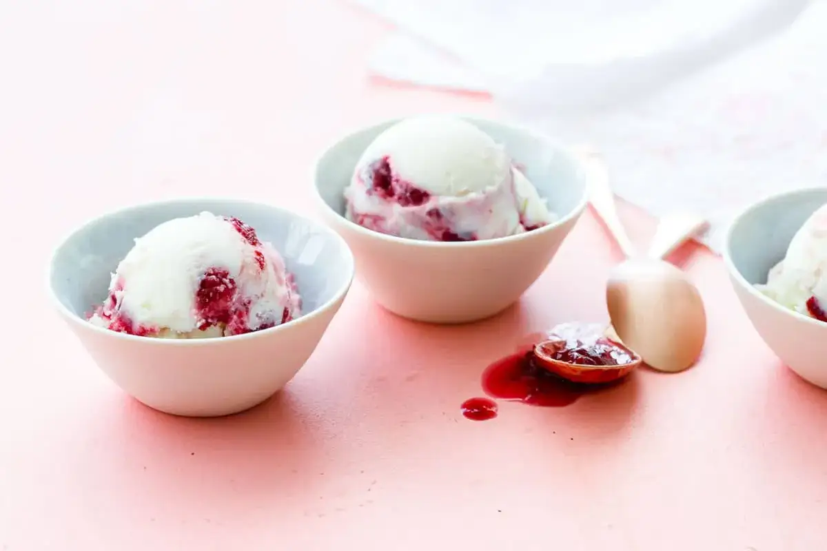 Drei Schalen mit cremigem Joghurt Kirsch Eis, garniert mit Kirschsauce. Ein L&ouml;ffel mit Kirschsauce liegt daneben.