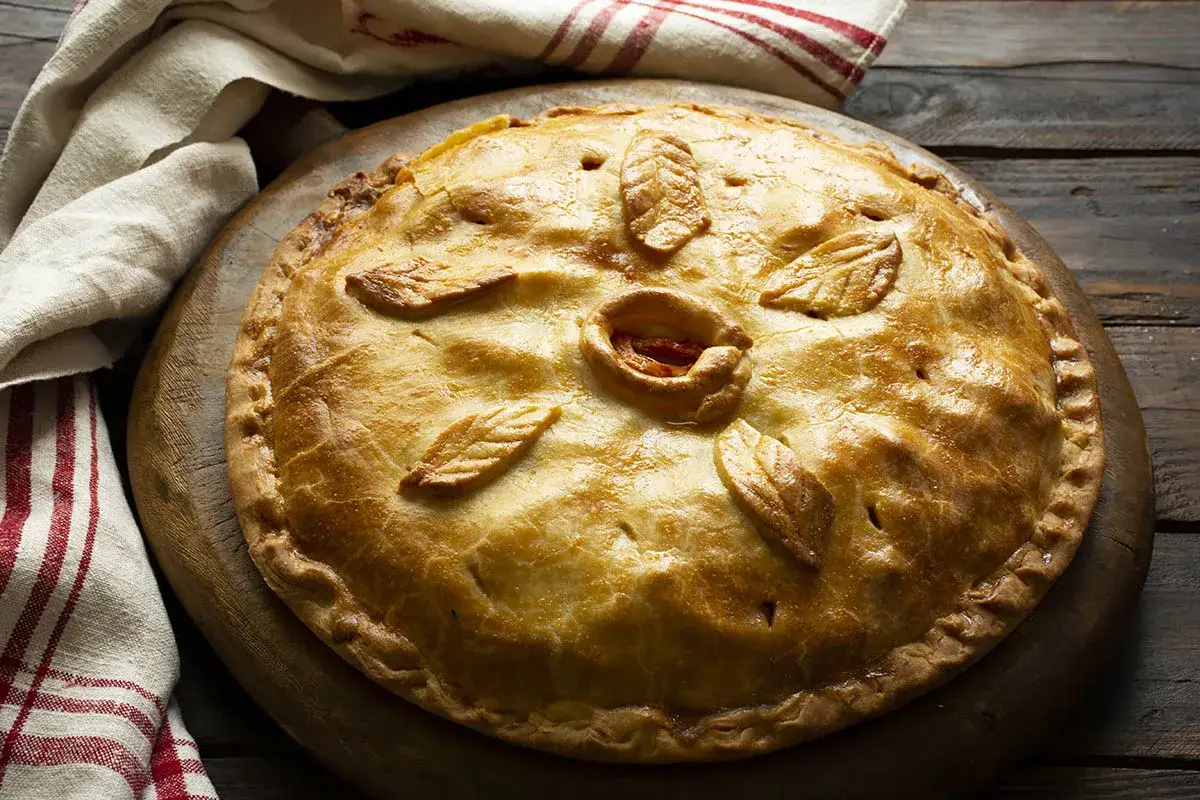 Empanada de pollo y setas dorada, decorada con hojas de masa y un centro circular, lista para ser servida.