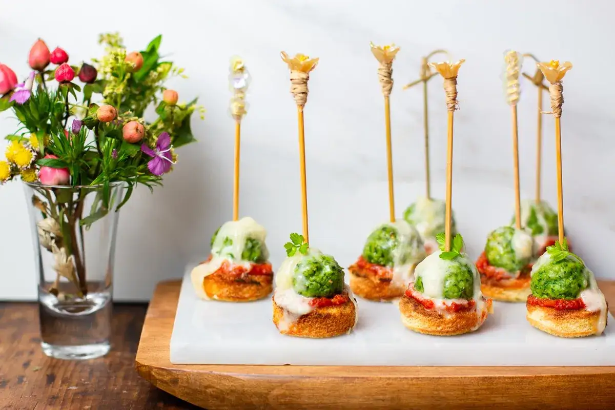 Verrines ap&eacute;ro : petites bouch&eacute;es sur toasts grill&eacute;s, garnies de sauce tomate, boulettes vertes et fromage fondu, d&eacute;cor&eacute;es de brochettes fleuries.