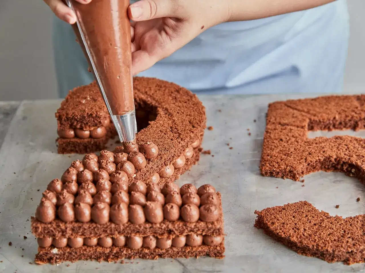 Schokoladen-Number-Cake wird mit Schokoladencreme verziert. Die Zahl 2 ist fast fertig, die Zahl 5 wartet noch.