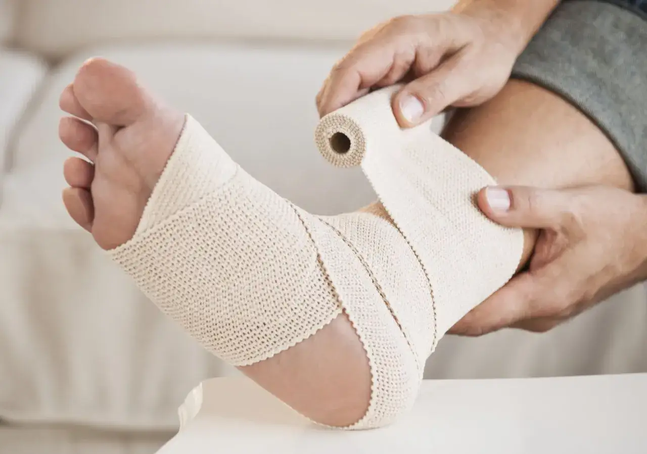 A person wraps an elastic bandage around their ankle. This compression may help with inflammation.