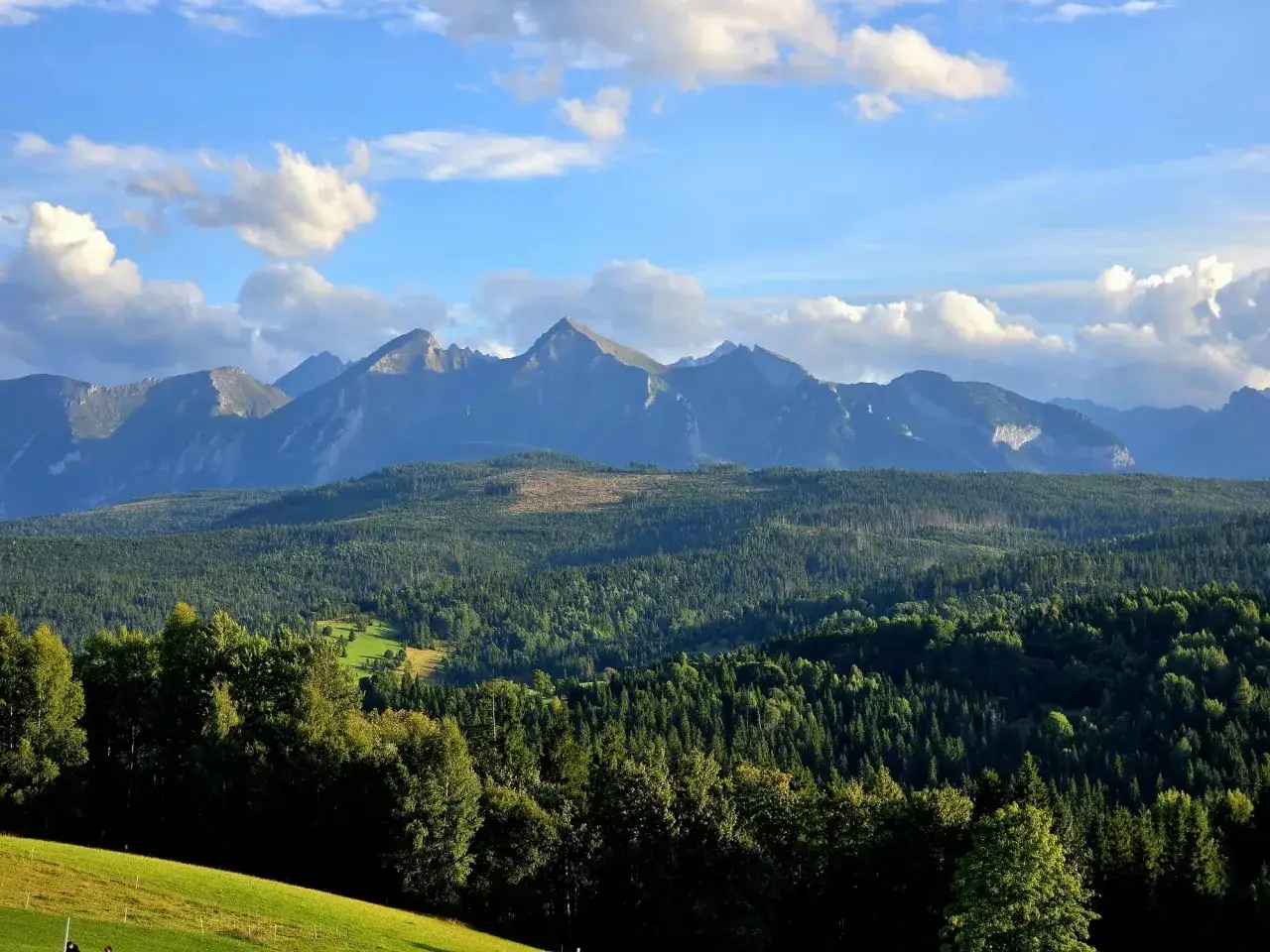 Widok na Tatry z przełęczy nad Łapszanką. Majestatyczne szczyty górskie na tle błękitnego nieba z chmurami.