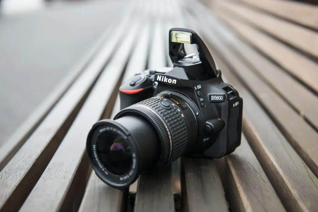 Nikon D5600 test na ławce. Aparat z obiektywem i wysuniętą lampą błyskową.