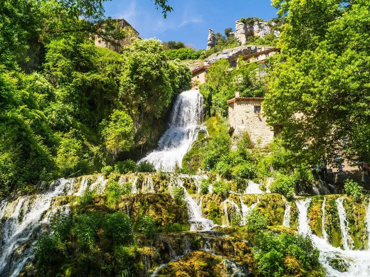 Cascadas de Espa&ntilde;a: un pueblo de piedra se aferra a la ladera verde junto a una cascada en terrazas.