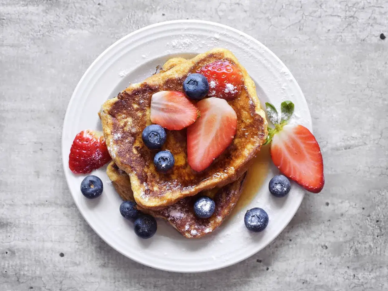 Délicieux pain perdu garni de fraises et myrtilles, saupoudré de sucre glace. Un régal pour les yeux et les papilles.