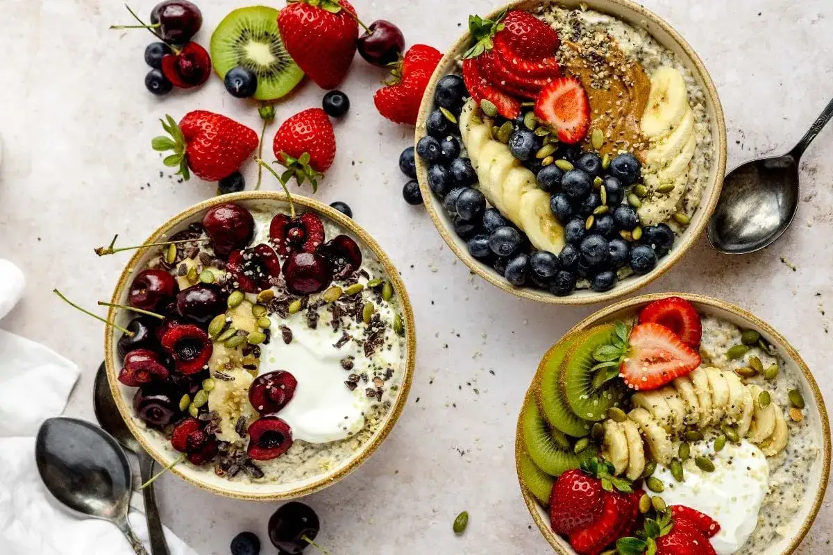 Drei Sch&uuml;sseln mit leckerem Porridge zubereiten, garniert mit frischen Beeren, Bananen, Kiwi und N&uuml;ssen. Ein gesunder Start in den Tag!