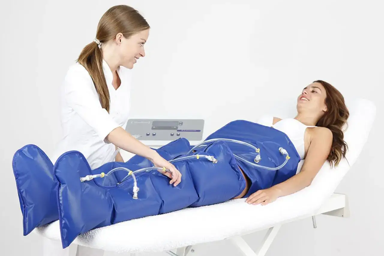Una donna in camice bianco controlla la pressoterapia su una paziente sdraiata. La pressoterapia aiuta a migliorare la circolazione.