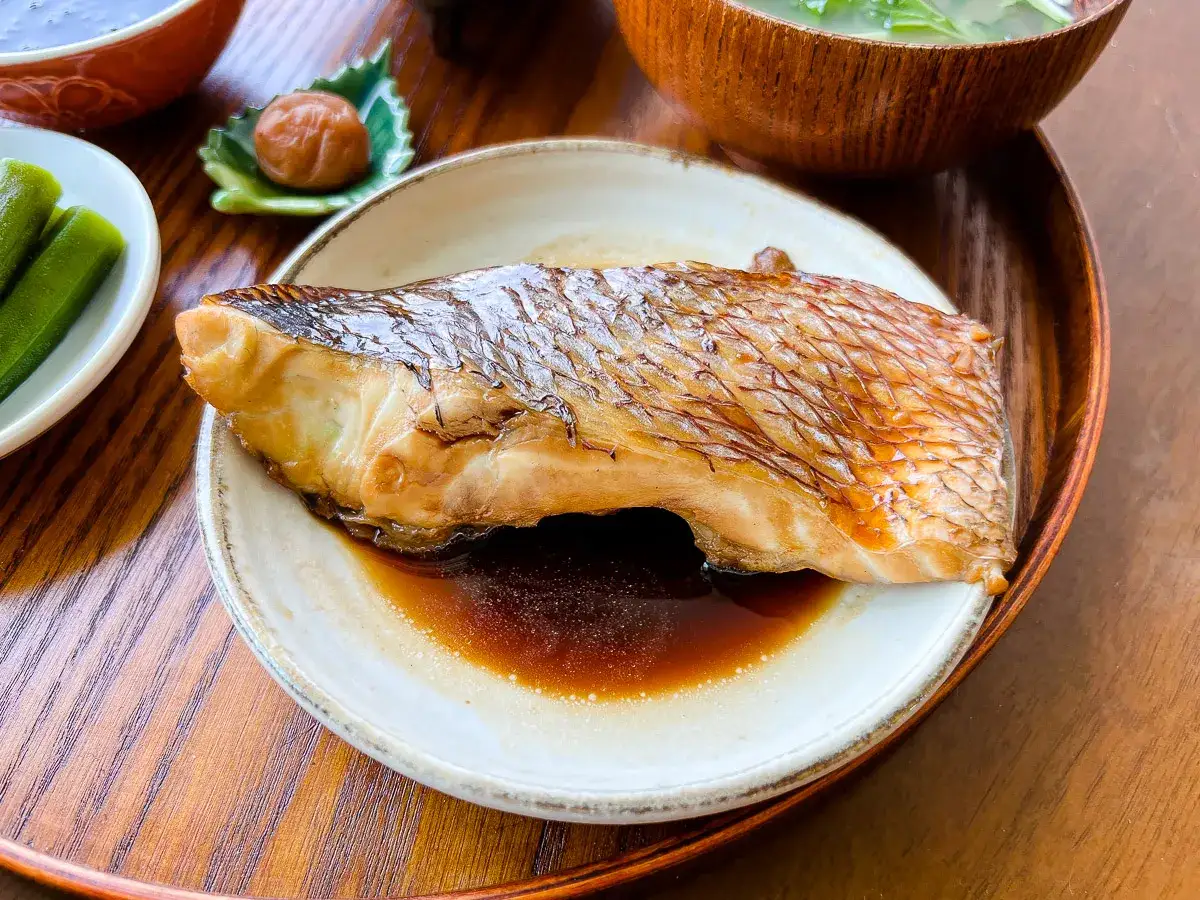 A perfectly cooked piece of karei no nitsuke, its skin crisp and golden, rests in a savory sauce. Served with pickled plum and okra.