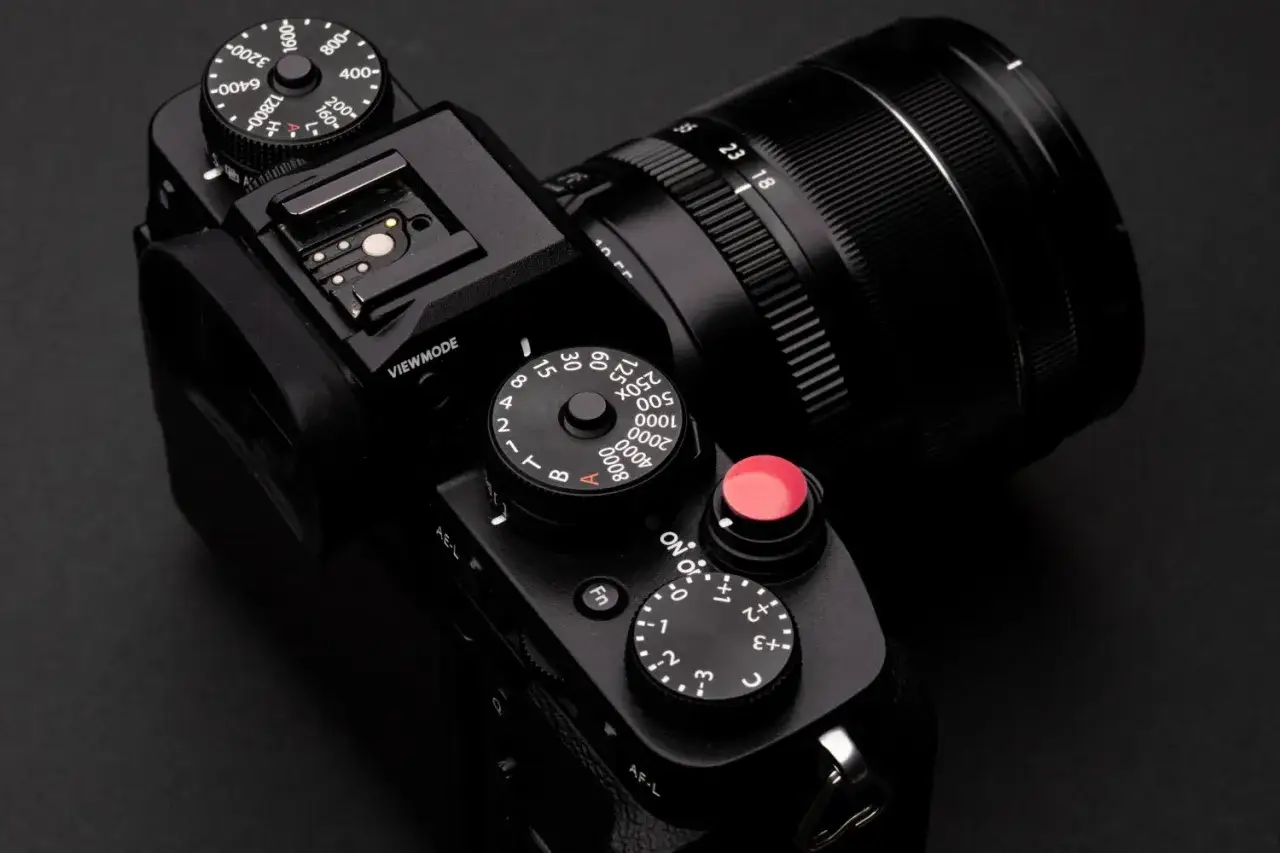 Macchina fotografica nera con obiettivo, mirino elettronico visibile, selettori per ISO, tempi e compensazione esposizione.