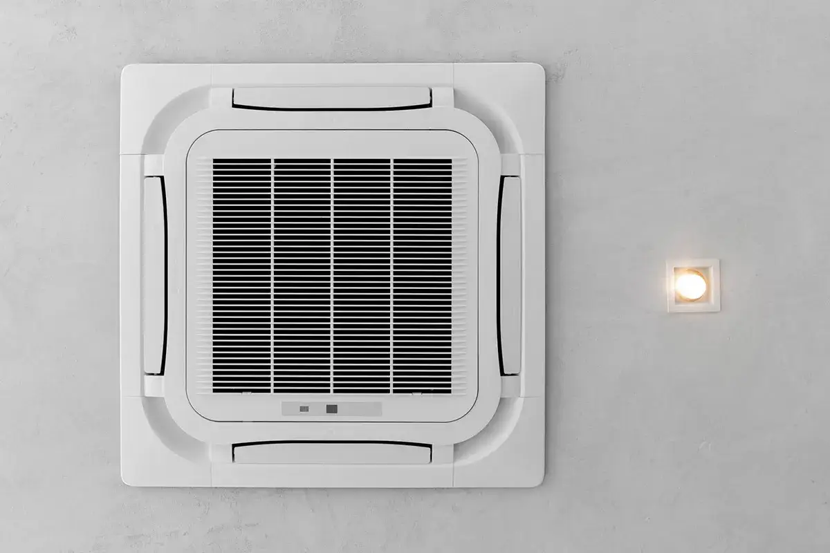 Kasetowa klimatyzacja na suficie obok kwadratowej lampy.