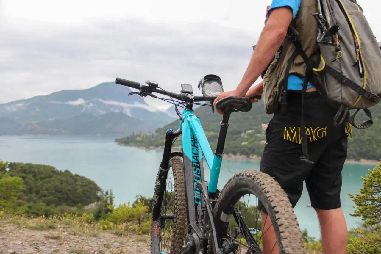 Un cycliste se tient à côté de son **vtt électrique débridable** bleu, prêt à explorer les montagnes et le lac.