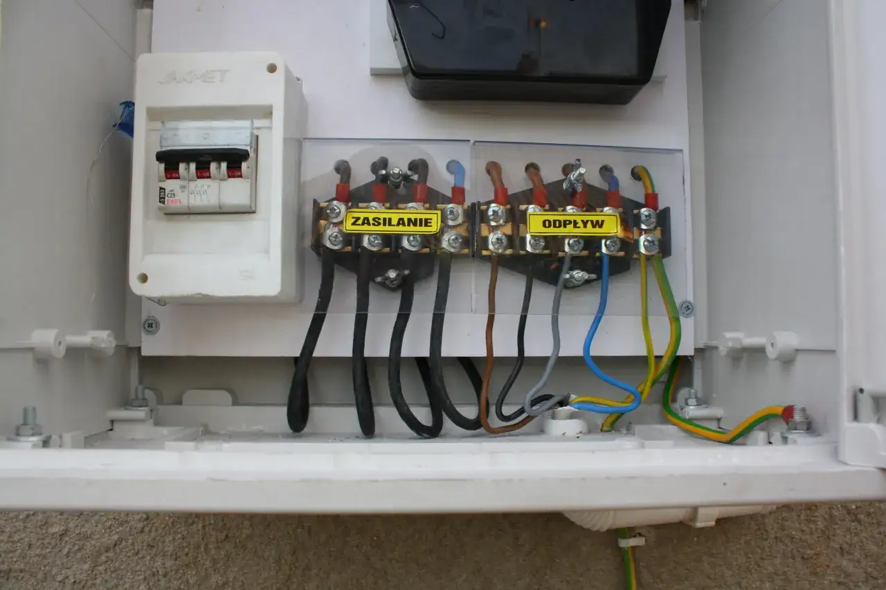 W skrzynce elektrycznej widać wyłącznik nadprądowy i listwy zaciskowe z etykietami 