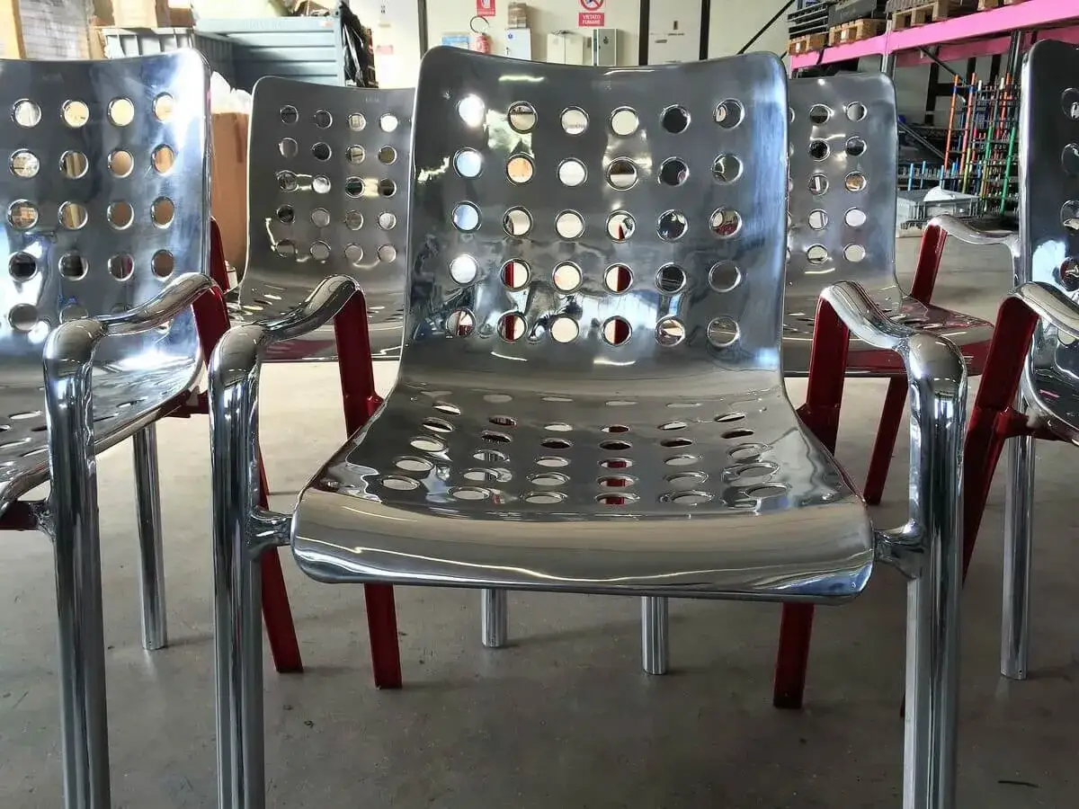Sedie moderne in metallo lucido con seduta traforata e gambe rosse. Riflettono la luce, mostrando cos'&egrave; il metallo nella sua essenza.