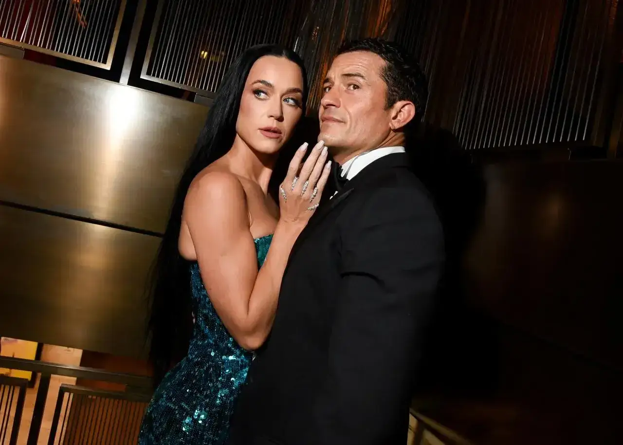 Katy Perry w błyszczącej sukni i Orlando Bloom w smokingu, czule obejmujący się na ściance.