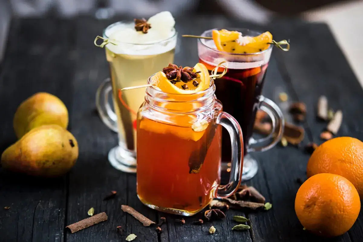 Trois boissons chaudes réconfortantes, dont une bière chaude épicée, garnies d'oranges et d'anis étoilé, sur fond de poires et d'épices.