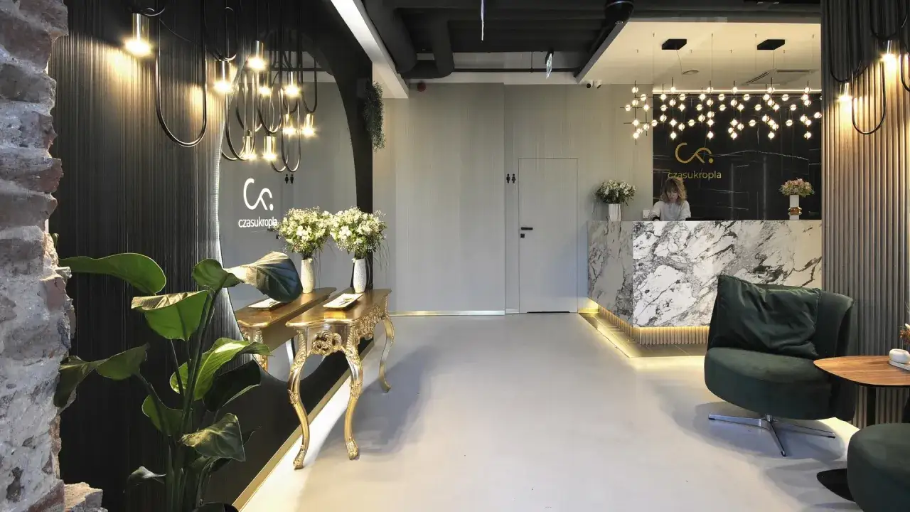 Nowoczesne wnętrze recepcji kliniki z marmurowym blatem, roślinami i designerskim oświetleniem.