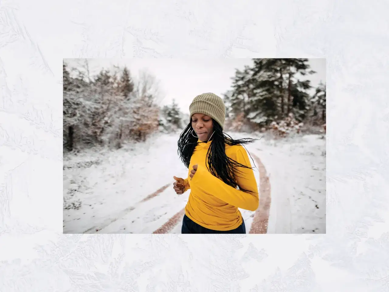 Frau läuft im Winter durch verschneiten Wald. Sie trägt eine gelbe Laufjacke und eine Mütze.