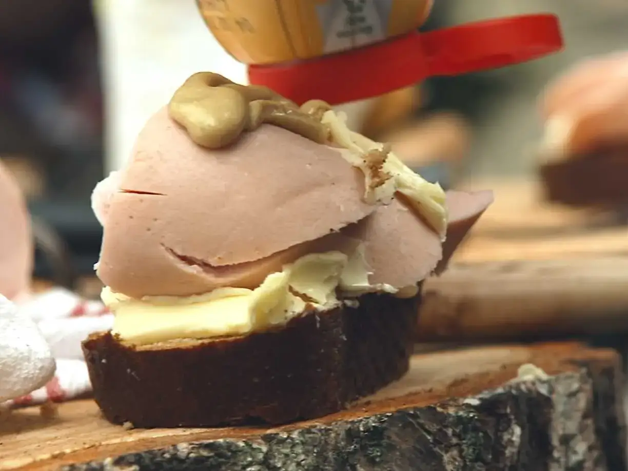 En klassisk jägarmacka med smör, falukorv och senap på mörkt bröd, redo att avnjutas.