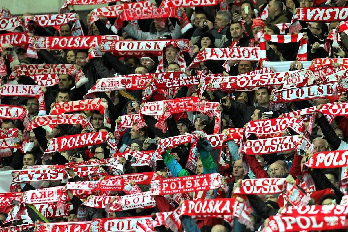 Tłum kibiców na meczu, trzymający biało-czerwone szaliki z napisem 