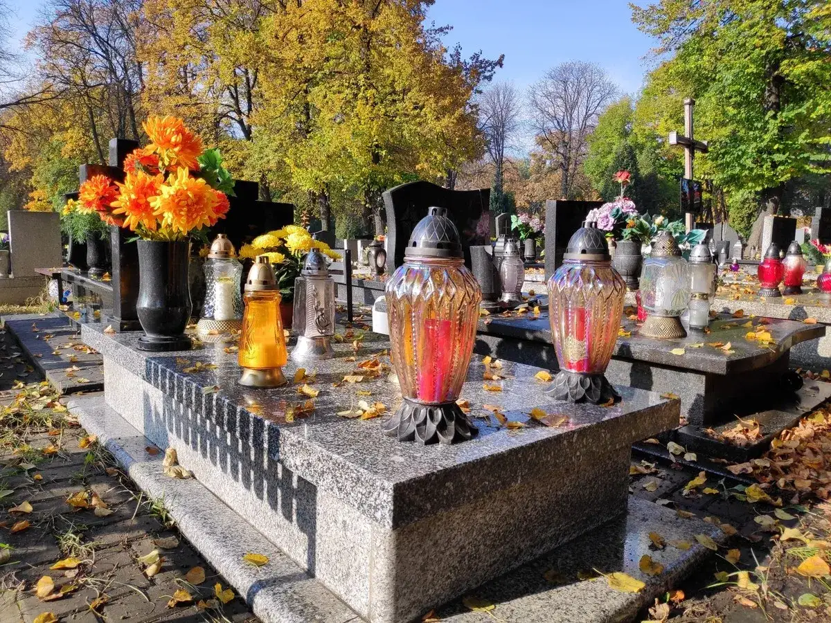 Nagrobki z kwiatami i zniczami. Jesienny krajobraz cmentarza. Różnica między cmentarzem komunalnym a parafialnym prawo i opłaty.