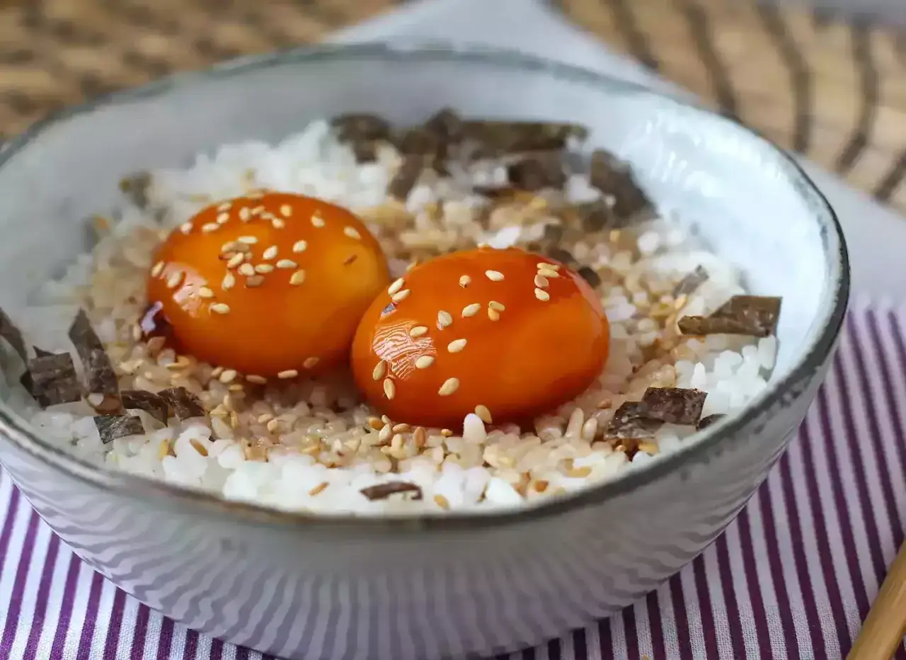 Un bol de riz blanc garni de deux jaunes d'oeuf marin&eacute; soja, parsem&eacute; de graines de s&eacute;same et d'algues.