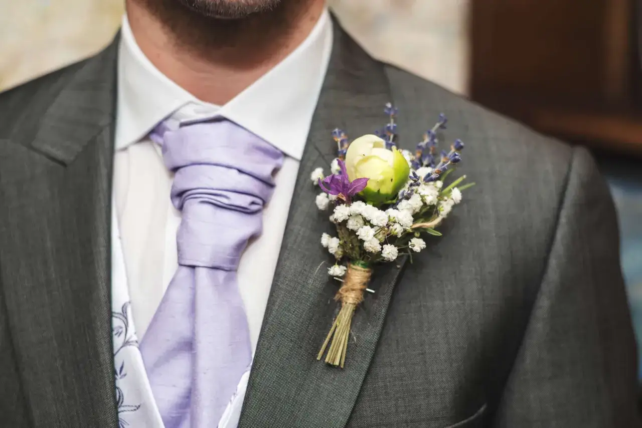 Elegancka butonierka w marynarce, ozdobiona delikatnymi kwiatami i lawendą, dodaje szyku stylizacji.