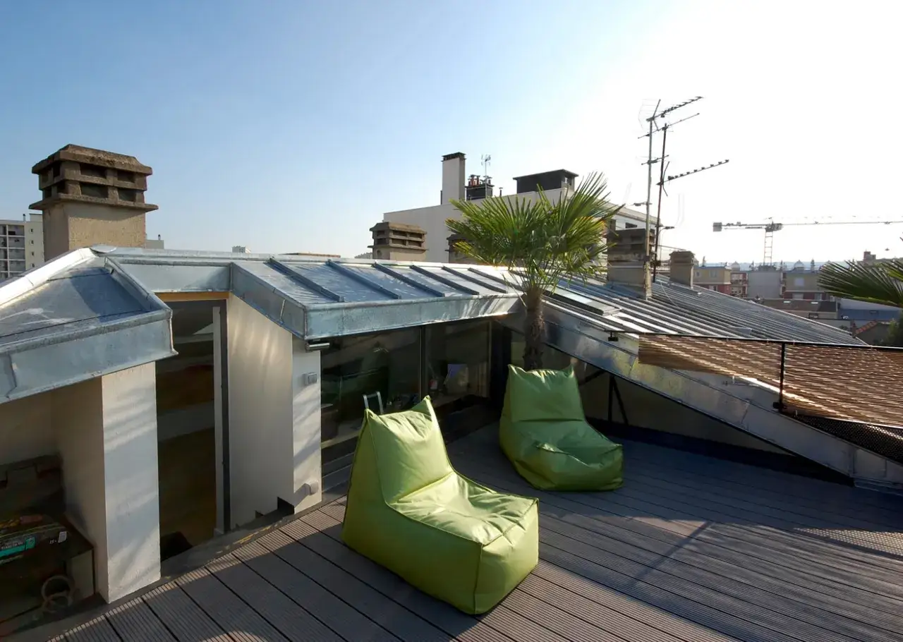 Aménagement toit terrasse avec autorisation : deux poufs verts et un palmier sur un deck en bois, vue sur les toits de Paris.