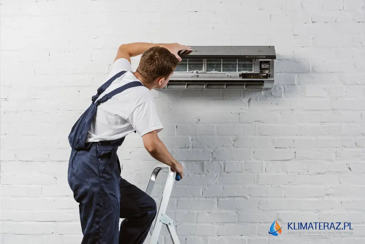 Technik w kombinezonie montuje klimatyzację na białej, ceglanej ścianie.