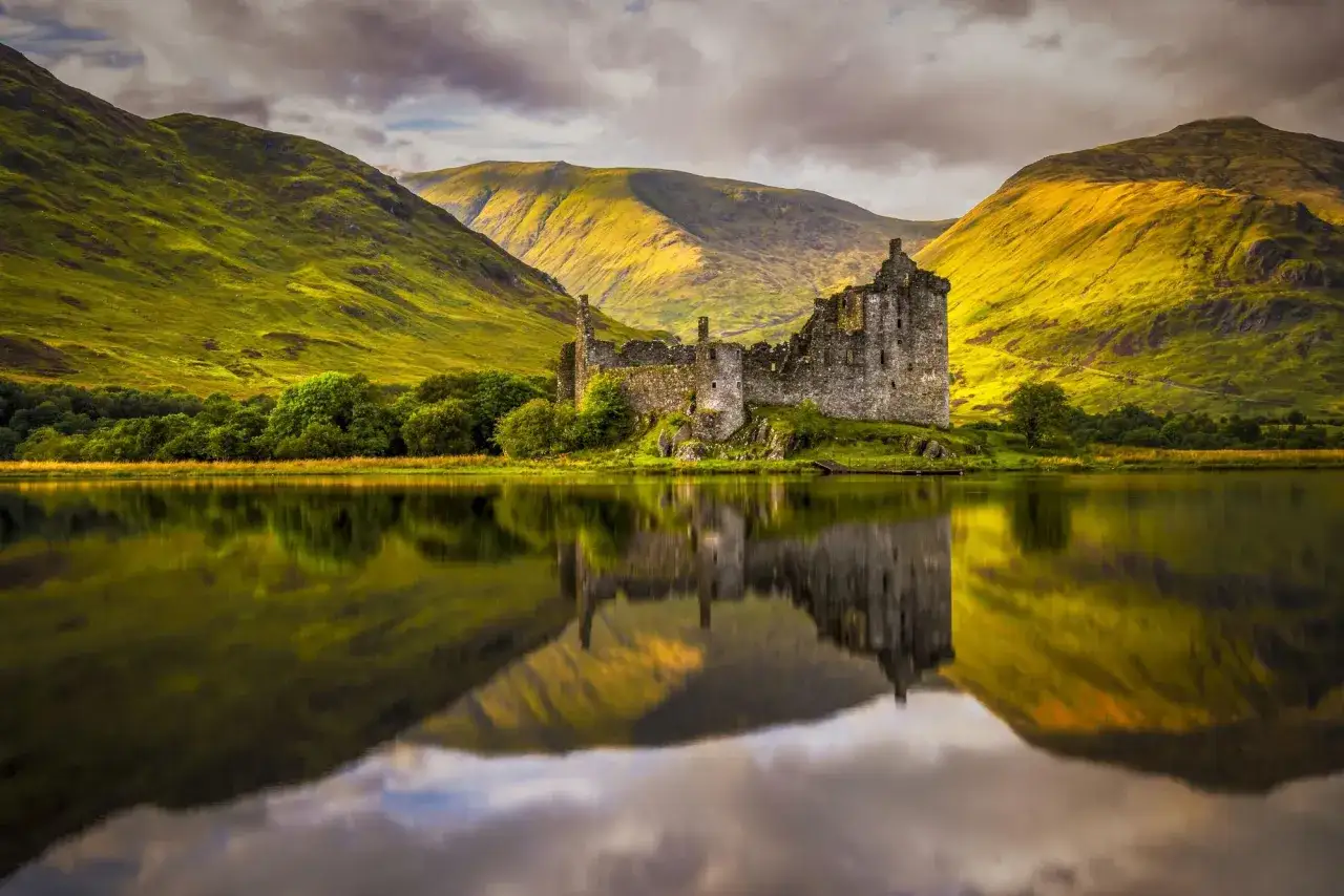Castillo en ruinas junto a un lago, reflejándose en el agua. Un paisaje idílico para tus viajes a Escocia.