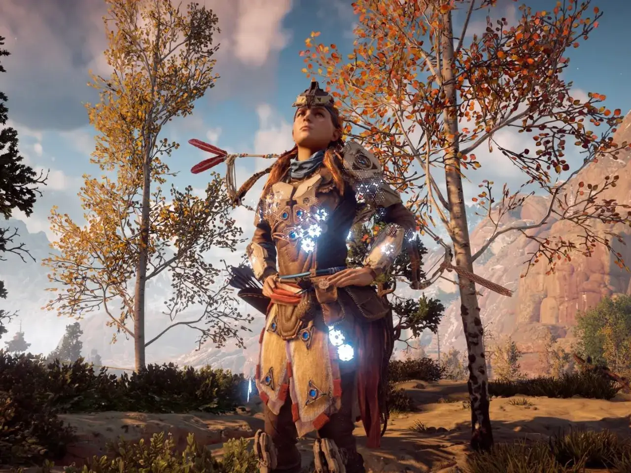 Aloy w zbroi z Horizon Zero Dawn, stojąca przed starożytną zbrojownią, otoczona jesiennymi drzewami.