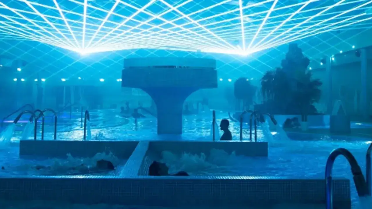 Un relajante spa de noche con luces azules y cascadas. Personas disfrutan del agua en un ambiente sereno.