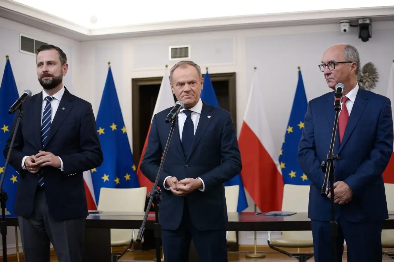 Trzech polityków w garniturach, na tle flag Polski i UE. Dyskusja o tym, do kiedy rządy PiS.
