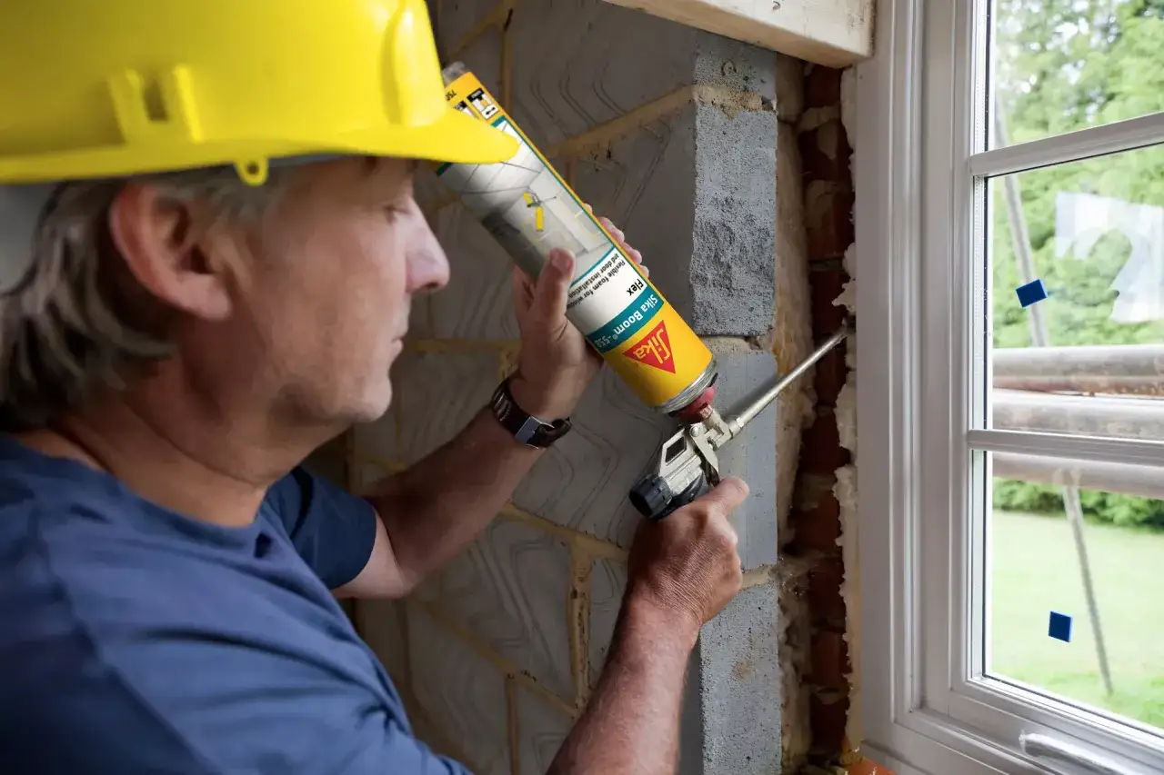 Obrero con casco amarillo aplica espuma expansiva para asegurar la estanqueidad al agua de las ventanas.