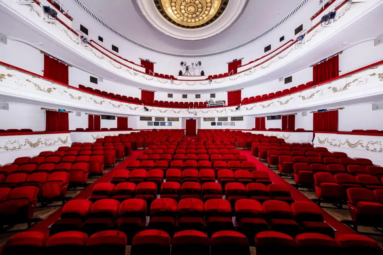 Widownia teatru dramatycznego w Warszawie, gotowa na kolejne spektakle z bogatego repertuaru. Czerwone fotele czekają na widzów.