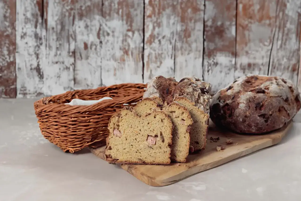 Frisch gebackenes Zwiebelbrot Rezept: Ein Laib und drei Scheiben auf einem Holzbrett, daneben ein Brotkorb.