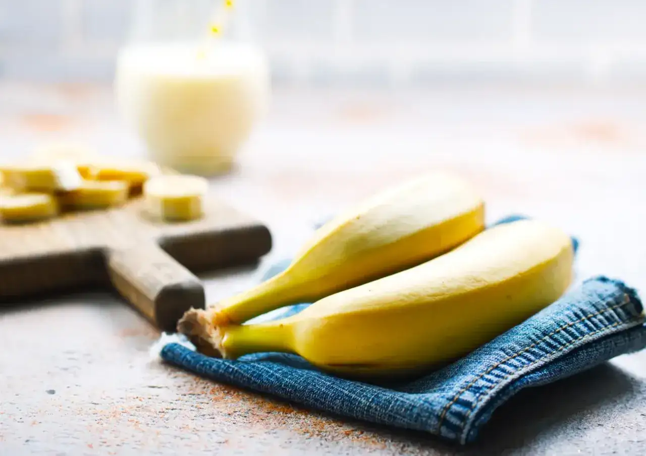 Dwa banany na dżinsowej serwetce, obok pokrojonych bananów i szklanki napoju. Czy cukrzyk może jeść banany? Tak, ale z umiarem.
