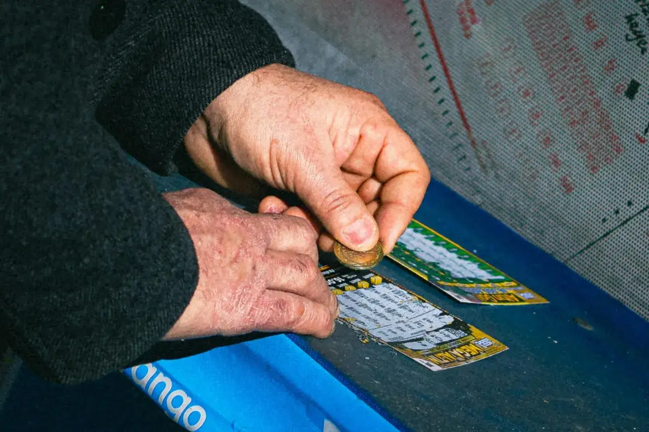 Dłoń z monetą zdrapuje zdrapkę, licząc na wygraną w jackpot.