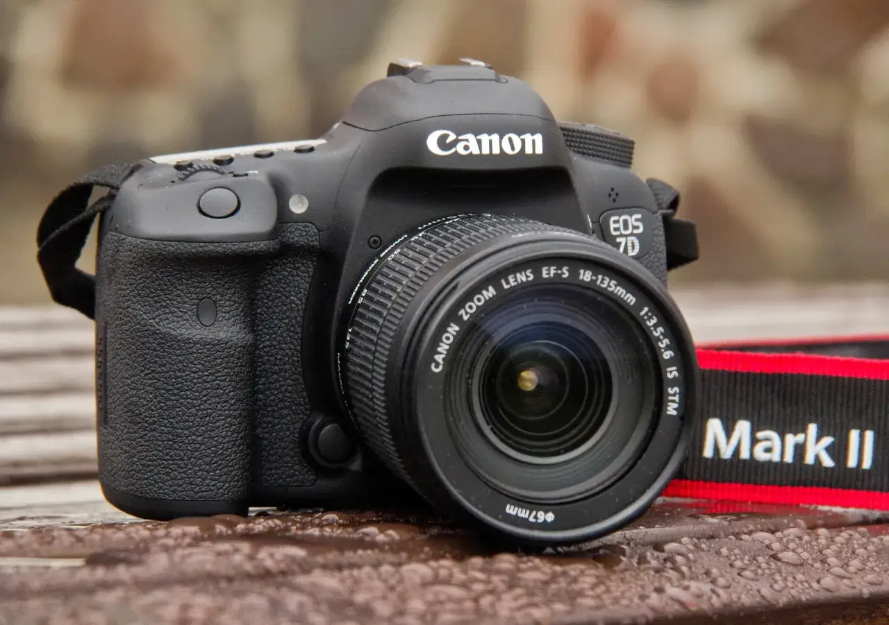 Czarny Canon EOS 7D z obiektywem EF-S 18-135mm na mokrym blacie. Pasek z napisem 