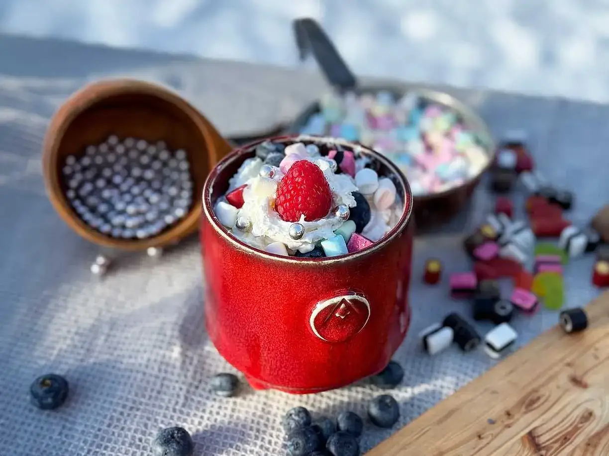 En röd mugg fylld med grädde, bär, marshmallows och godis. En perfekt varm choklad för en mysig stund.