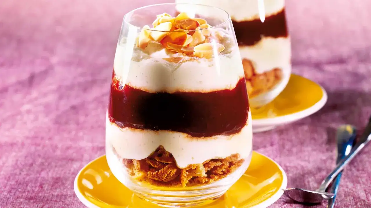 Schichtdessert im Glas mit knusprigen Keksen, cremiger Masse und Fruchtsoße, garniert mit Mandelblättchen. Ein köstliches Amarettini Dessert.